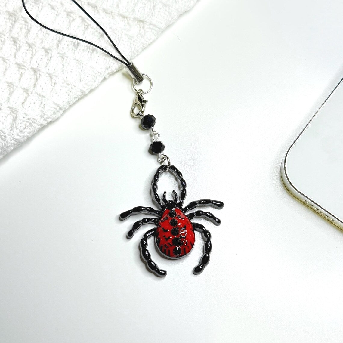 Spider-shaped phone charm with red and black design on a white surface