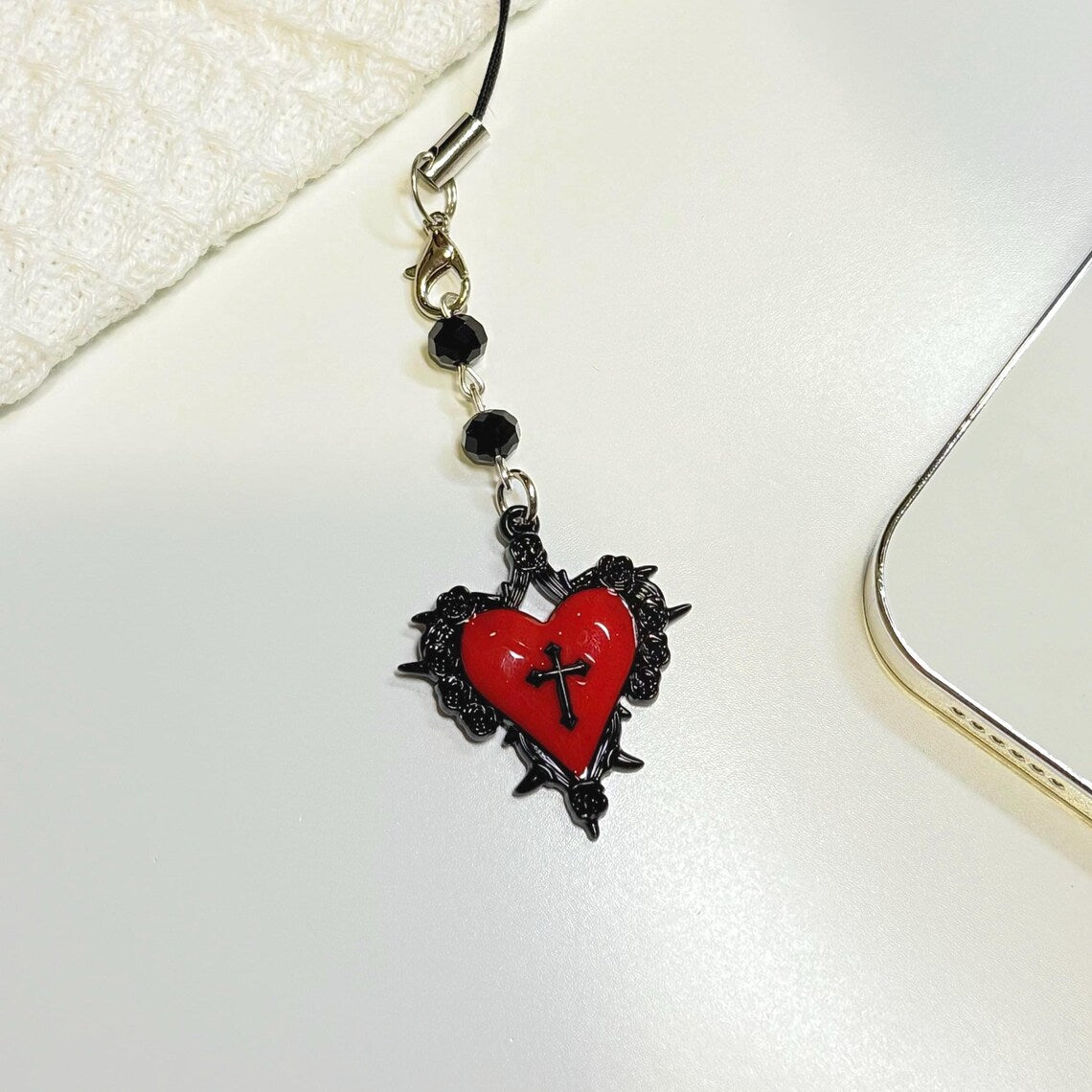 Red heart-shaped pendant with black details and a cross on a white surface
