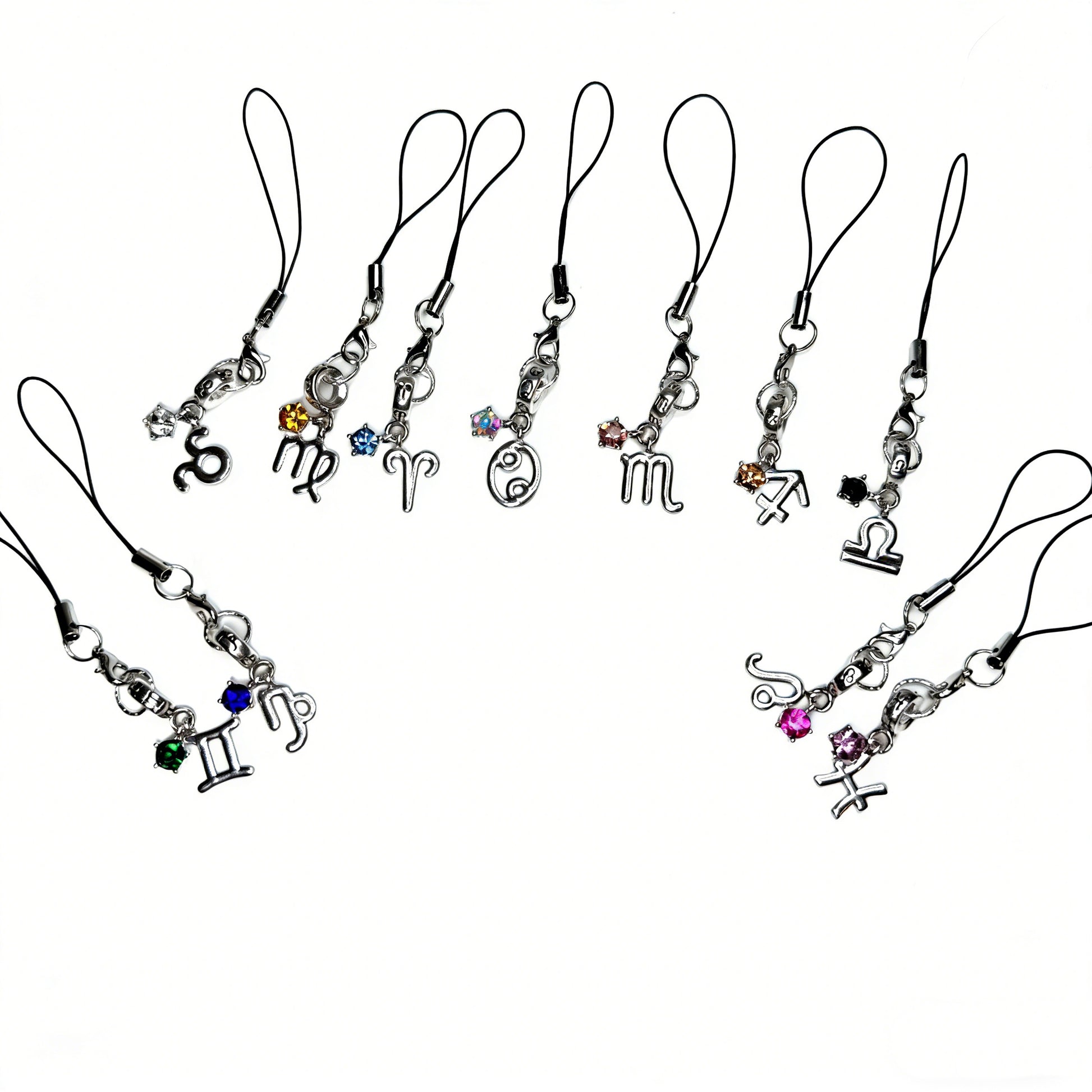 A collection of handmade silver zodiac phone charms including Scorpio, Virgo, Aries, Cancer, and Gemini with colorful crystals by Case not Cake.