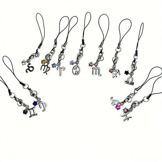 A collection of handmade silver zodiac phone charms including Scorpio, Virgo, Aries, Cancer, and Gemini with colorful crystals by Case not Cake.